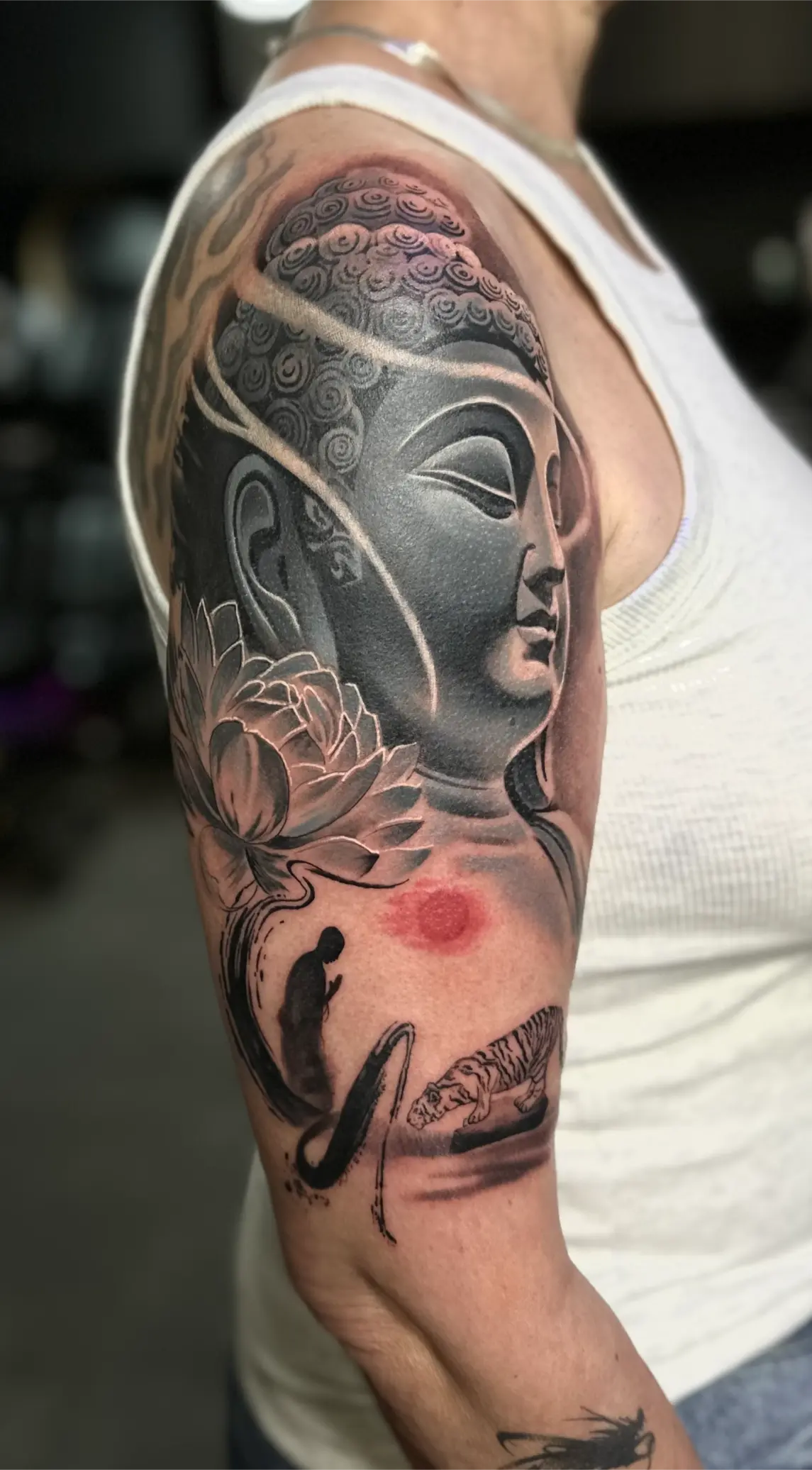 Tatouage FineLine Tattoo sur bras, représentant Bouddha, lotus et tigre, style artistique en noir et gris.